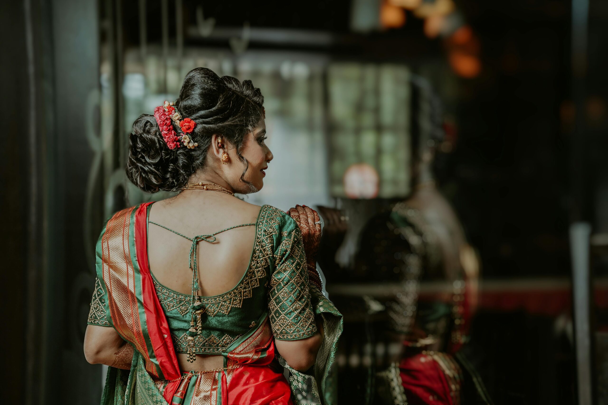 Back view of a woman in a traditional saree with ornate hairstyle, reflecting.