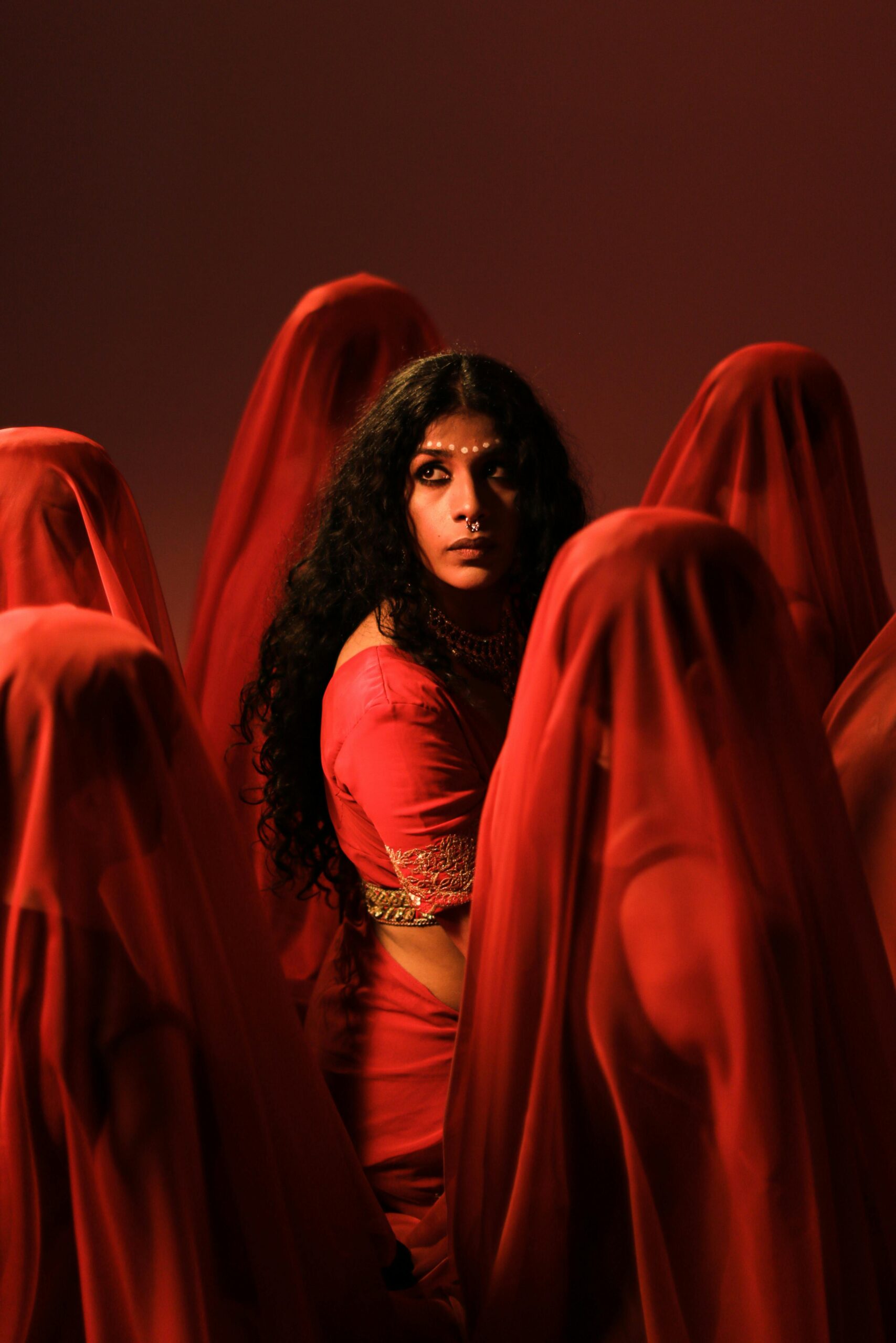 Indian woman in traditional attire surrounded by veiled figures in red. As Kollam Wedding Dress Shop