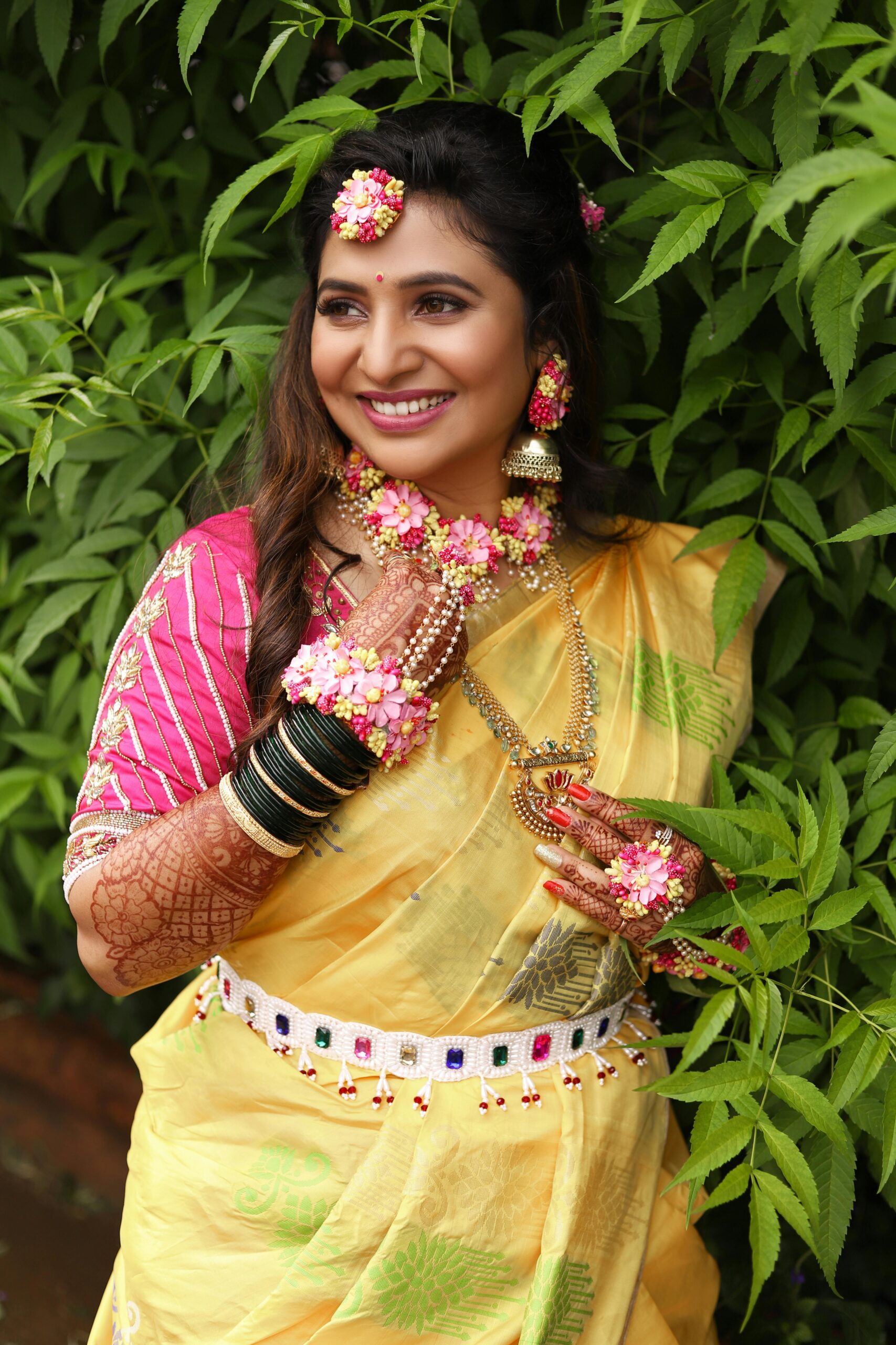 Smiling Indian woman in traditional attire surrounded by lush greenery.
