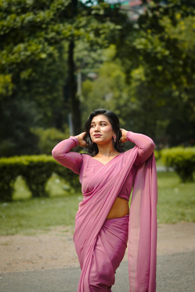 A beautiful woman poses confidently outdoors in a vibrant pink saree, exuding grace and poise.