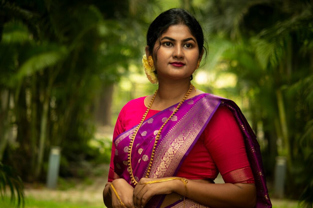 Elegant portrait of a South Asian woman in traditional Indian saree in a lush outdoor setting.