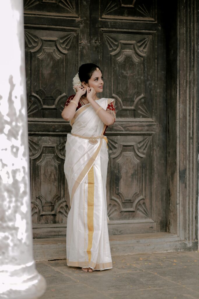 A woman in a traditional Indian saree adjusts her hair in front of an ornate wooden door.