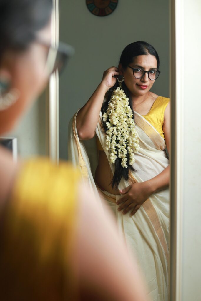 Indian woman wearing traditional saree with gajra, posing indoors looking in mirror.