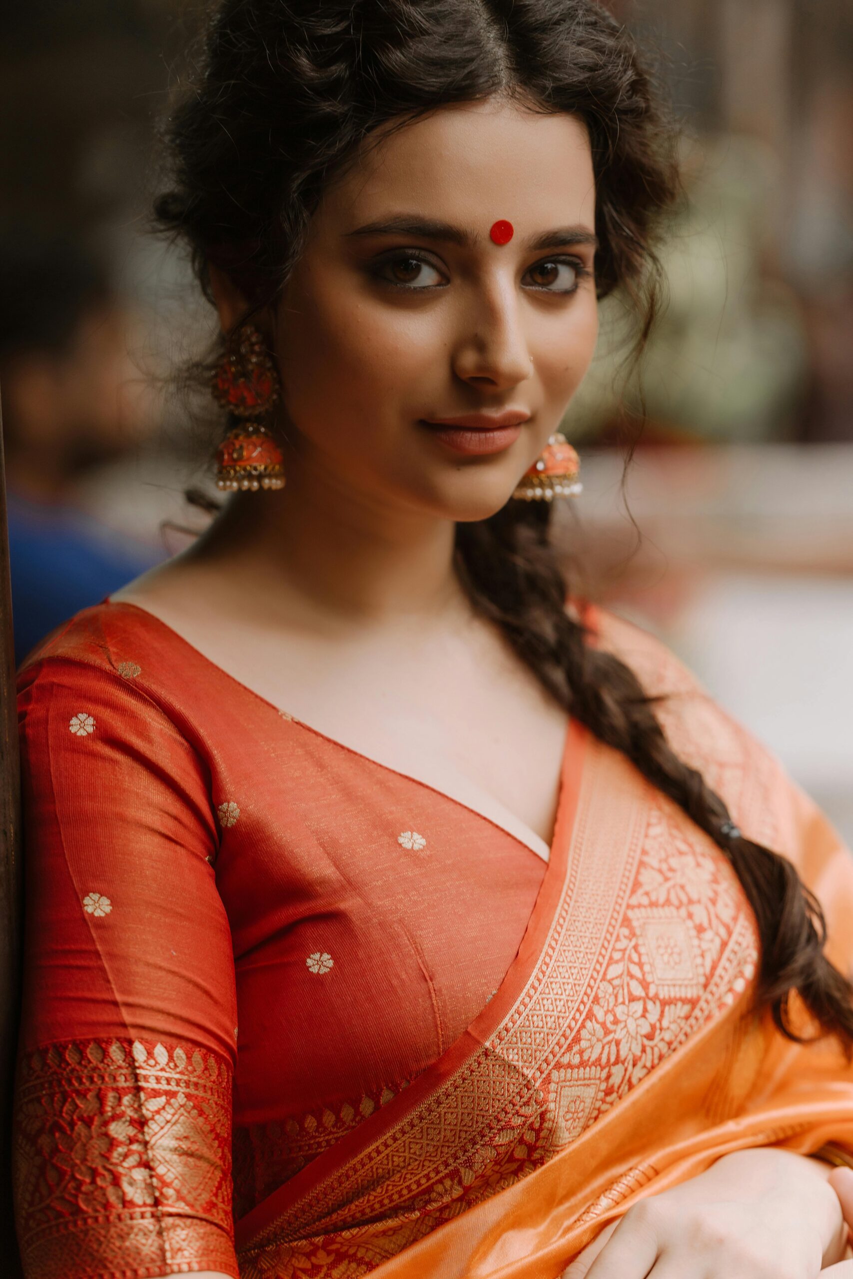 Portrait of a woman in an orange traditional saree with intricate patterns.