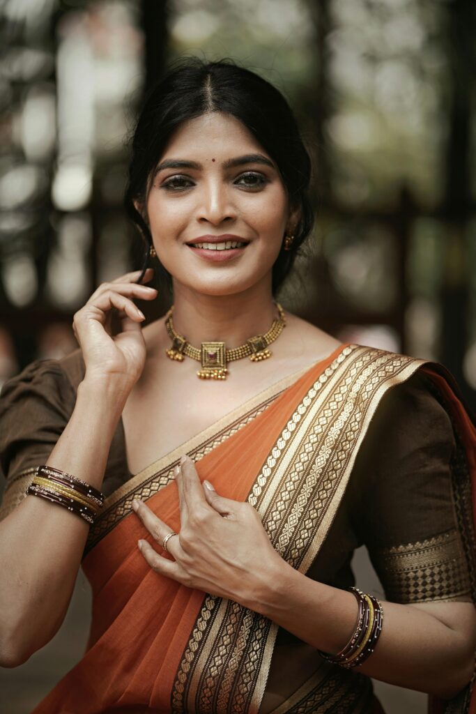 Elegant portrait of a smiling woman in a traditional Indian saree and jewelry outdoors.