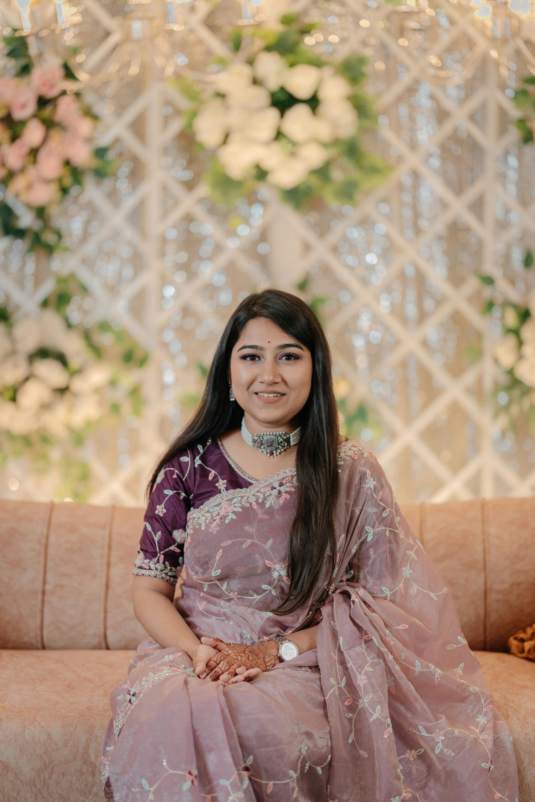 Portrait of a woman in traditional Indian attire with floral backdrop, exuding grace and elegance.