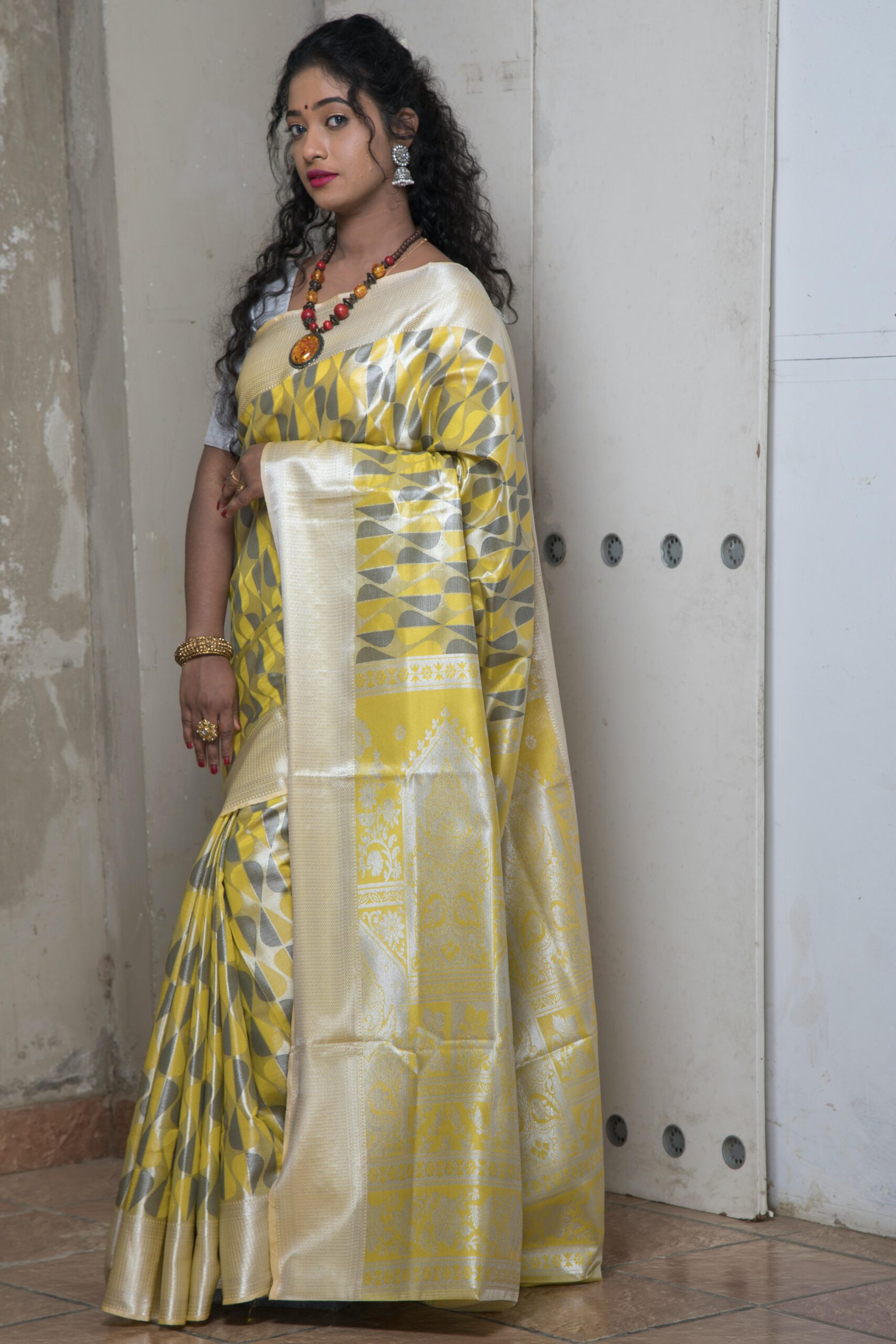 A woman in a yellow saree poses elegantly indoors, showcasing traditional fashion.