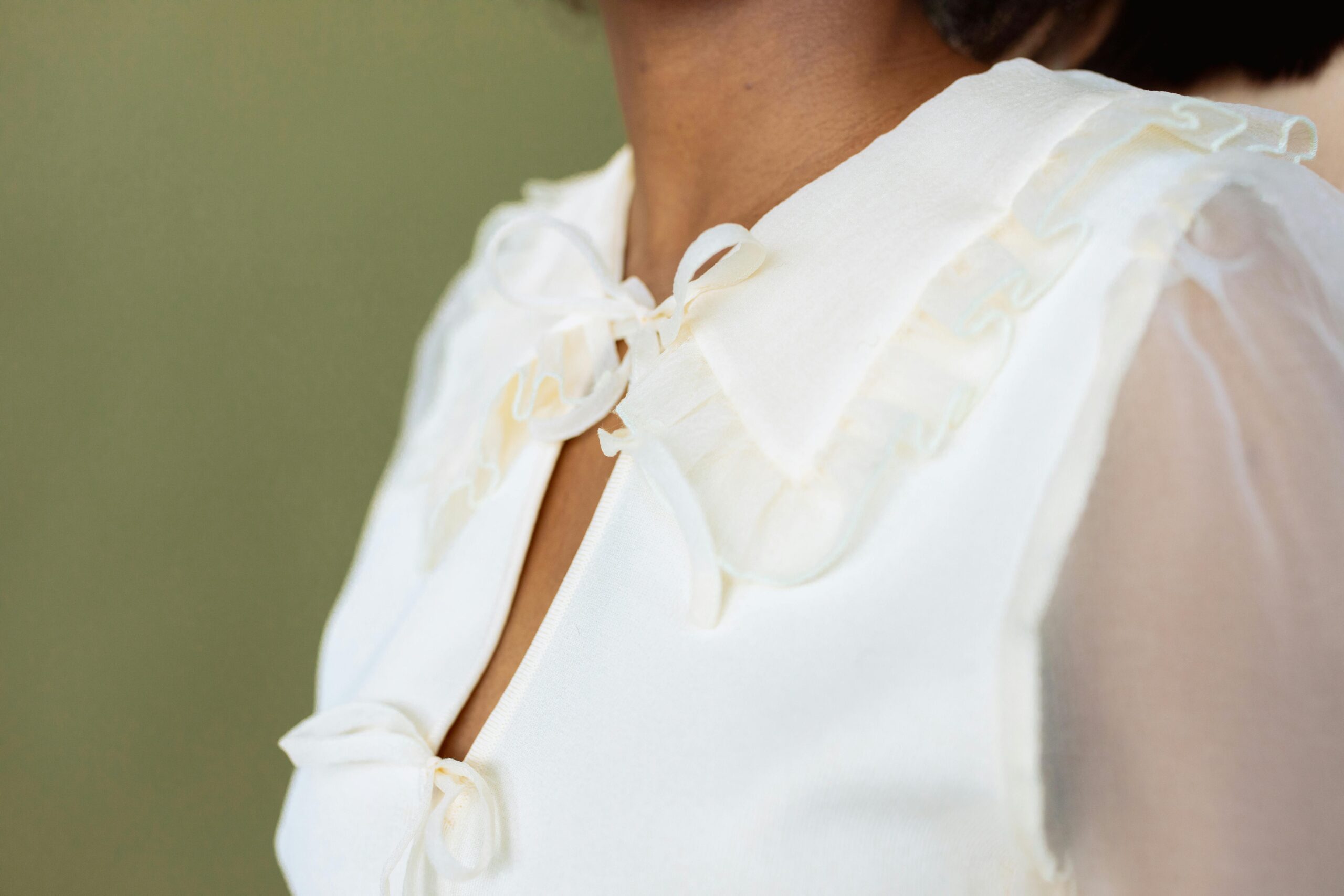 Close view of a person wearing an elegant white blouse with a delicate ribbon detail.